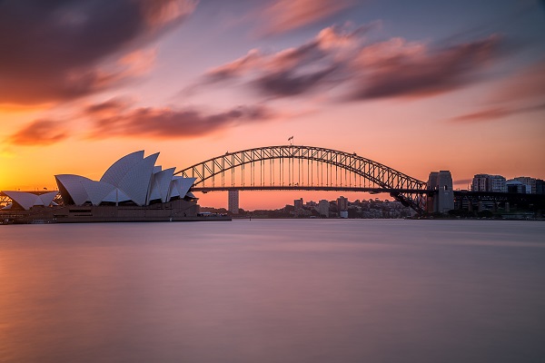 A beautiful shot of the Sydney harbor bridge with a light pink and blue sky in the background at sunset